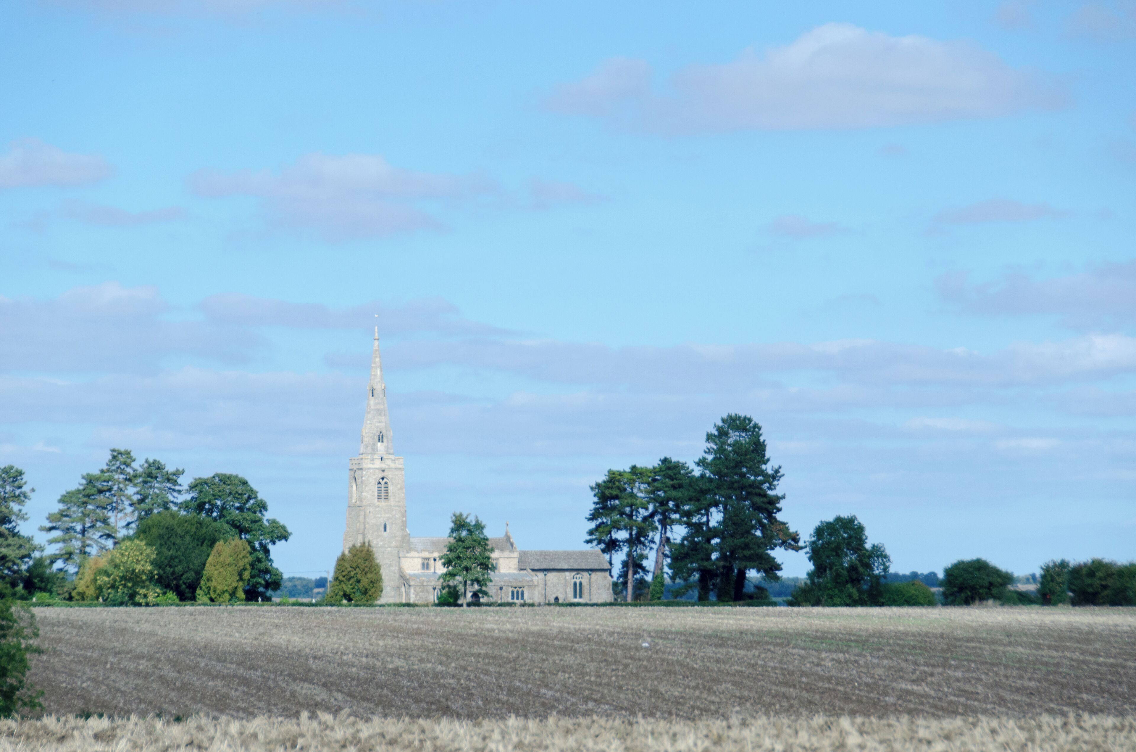 A church with a tall tower, surrounded by fields and trees.