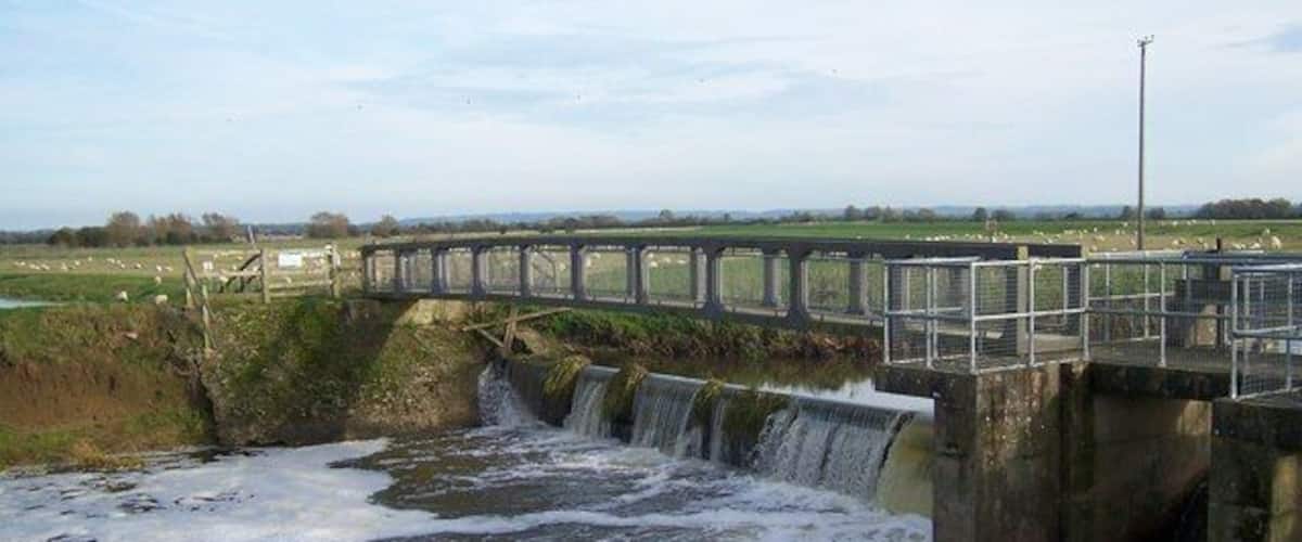 A concrete dam with a small waterfall and a metal bridge over it.