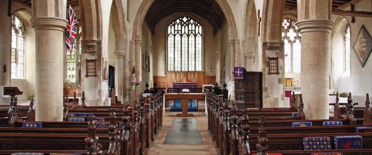 An interior of a church with wooden pews, stone columns, and stained glass windows.