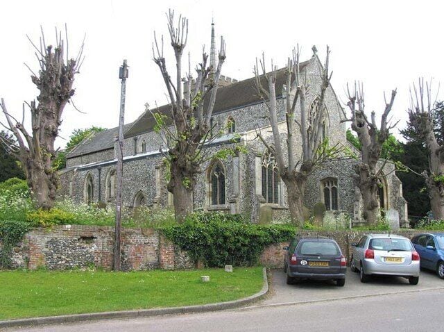 A stone church with arched windows and a bell tower, surrounded by leafless trees and parked cars.