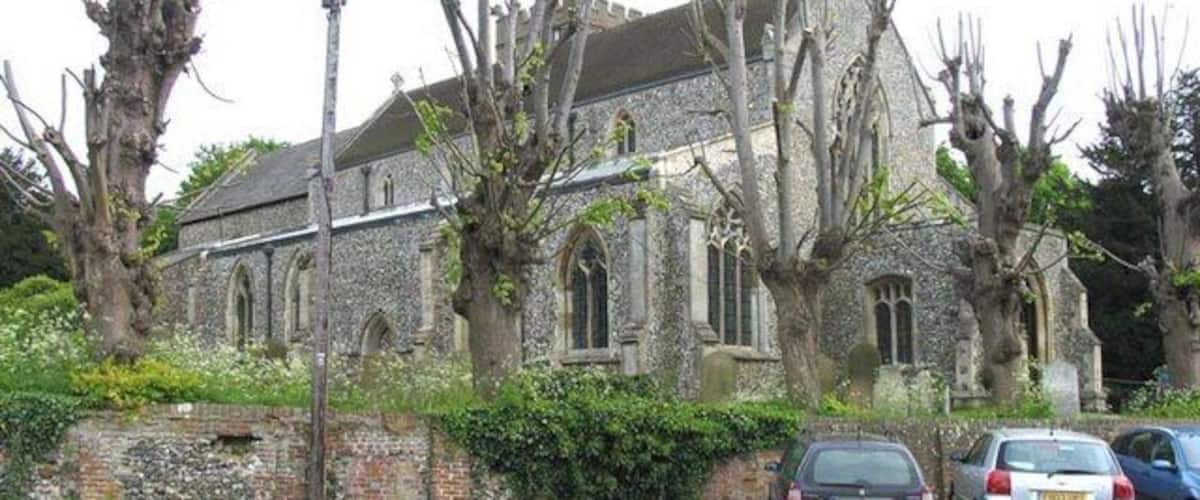A stone church with arched windows and a bell tower, surrounded by leafless trees and parked cars.