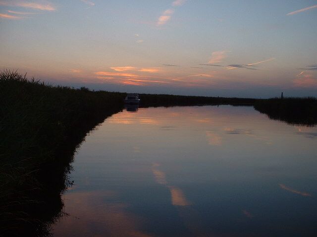 A calm river at dusk with a boat in the distance and a small structure on the horizon.