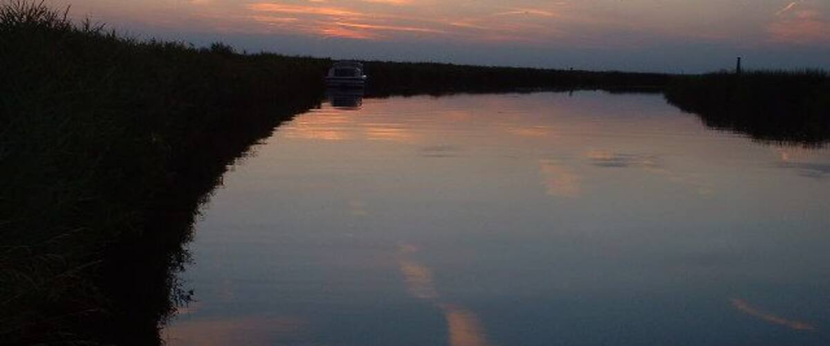 A calm river at dusk with a boat in the distance and a small structure on the horizon.
