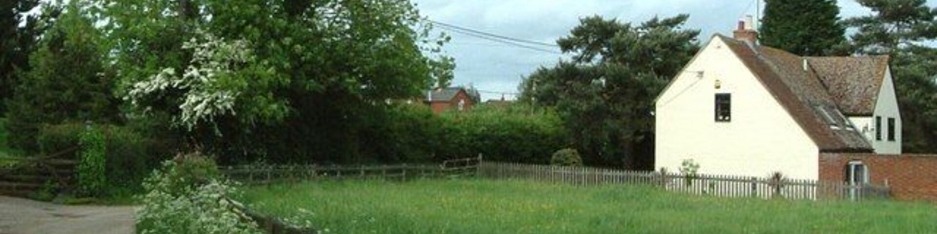 A rural landscape with a white house, a wooden fence, and a large tree.
