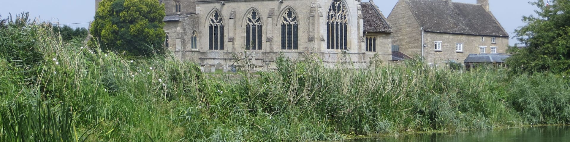 A historic building with arched windows and a tower, surrounded by a body of water and lush greenery.