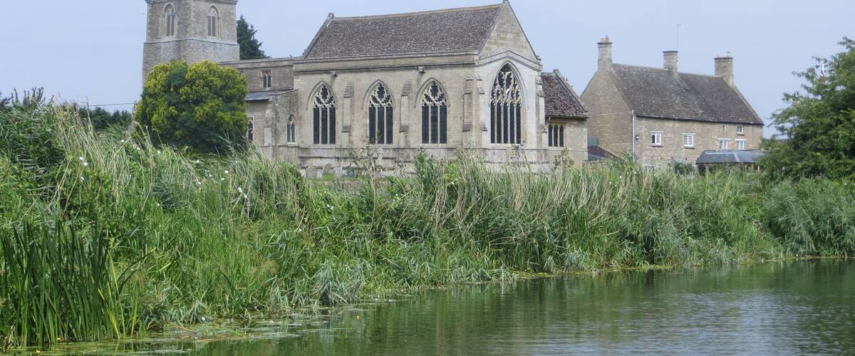 A historic building with arched windows and a tower, surrounded by a body of water and lush greenery.