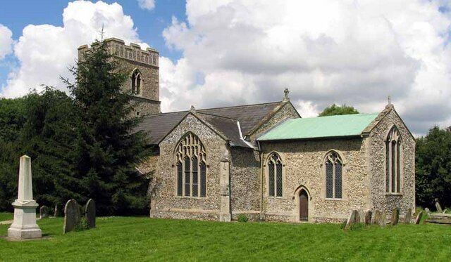 A stone church with a bell tower and a green roof, surrounded by a cemetery.