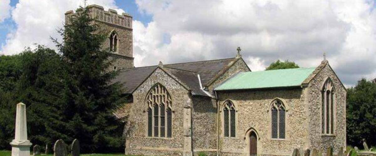 A stone church with a bell tower and a green roof, surrounded by a cemetery.