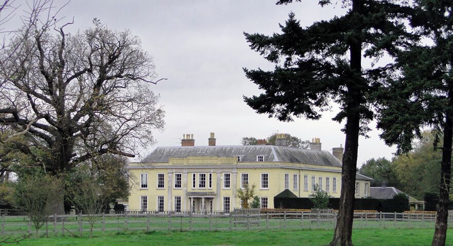 A large yellow building with a green lawn in front, surrounded by trees.