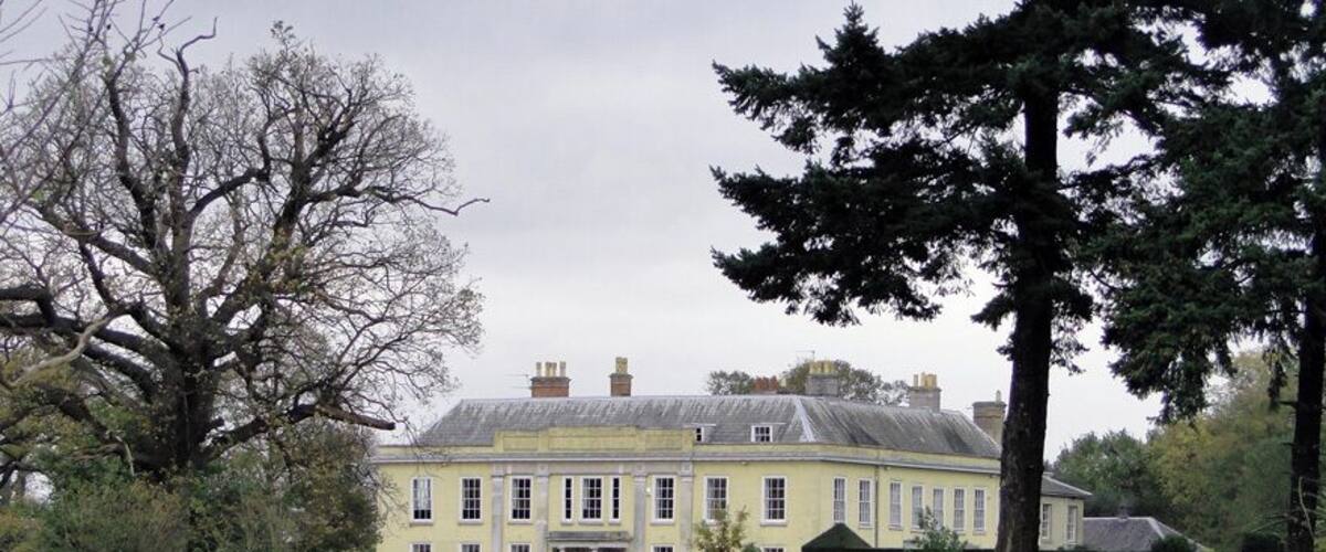 A large yellow building with a green lawn in front, surrounded by trees.