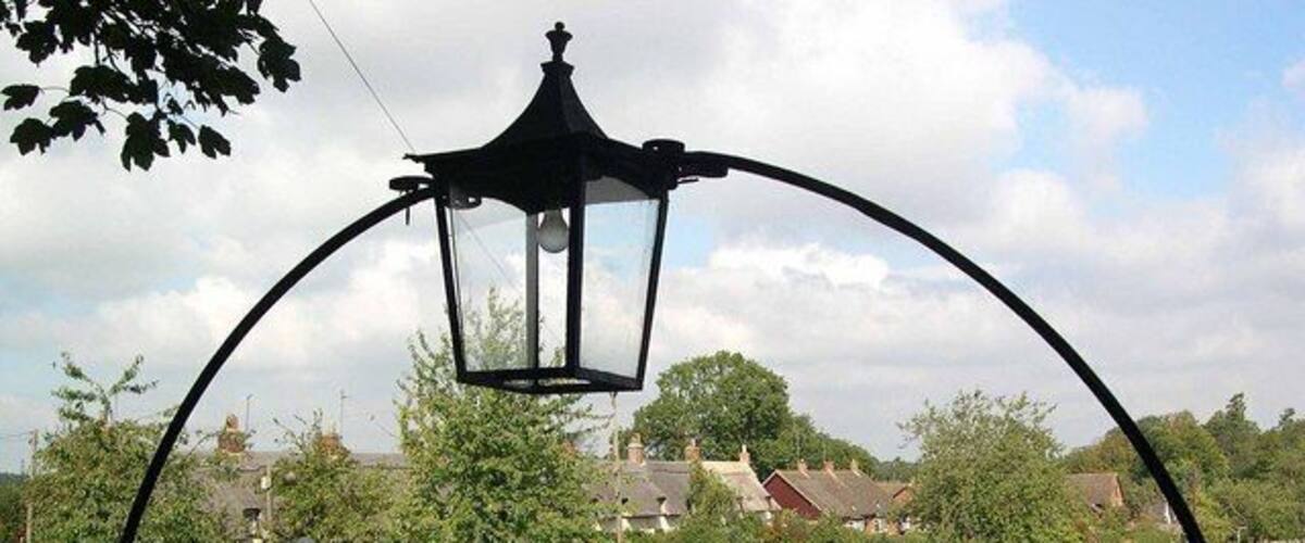 A park with a black metal lamp post, a paved path, and houses in the background.