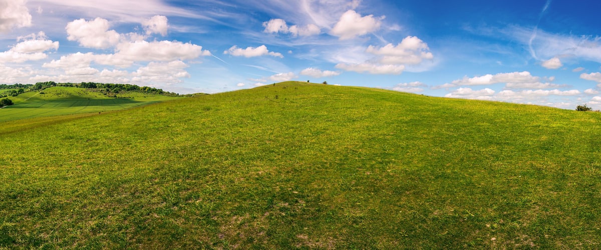 A green hill with a clear sky and scattered clouds.
