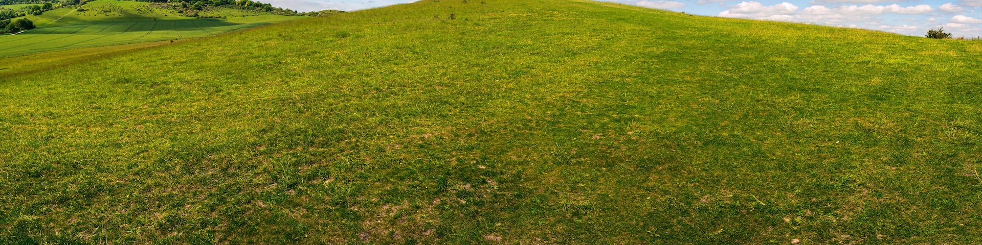 A green hill with a clear sky and scattered clouds.