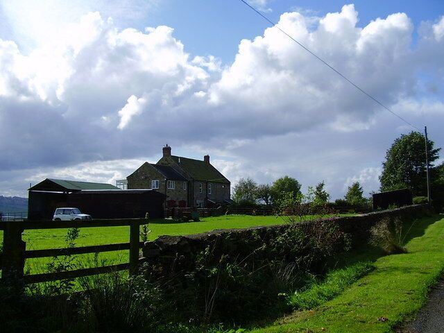A rural landscape with a stone wall, a green field, and a house with a green roof.