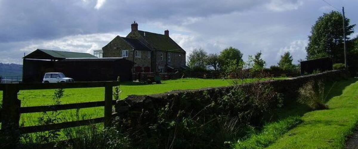 A rural landscape with a stone wall, a green field, and a house with a green roof.