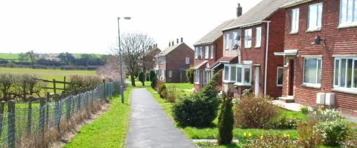 A residential street with houses, a paved path, and a fenced field.