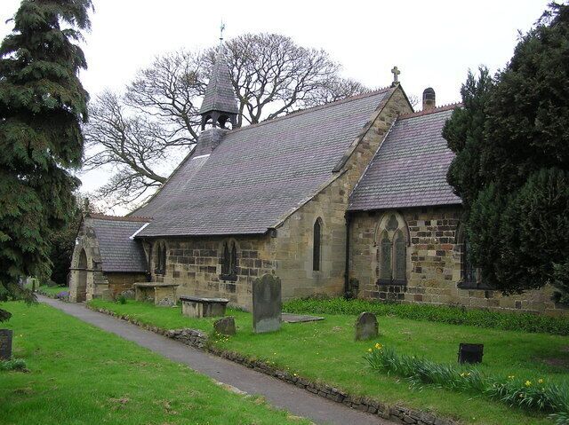 A stone church with a bell tower, surrounded by a cemetery with headstones and a pathway.