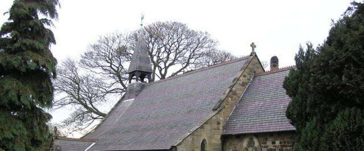 A stone church with a bell tower, surrounded by a cemetery with headstones and a pathway.