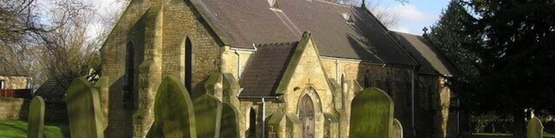 A church with a tall steeple and a graveyard with headstones.