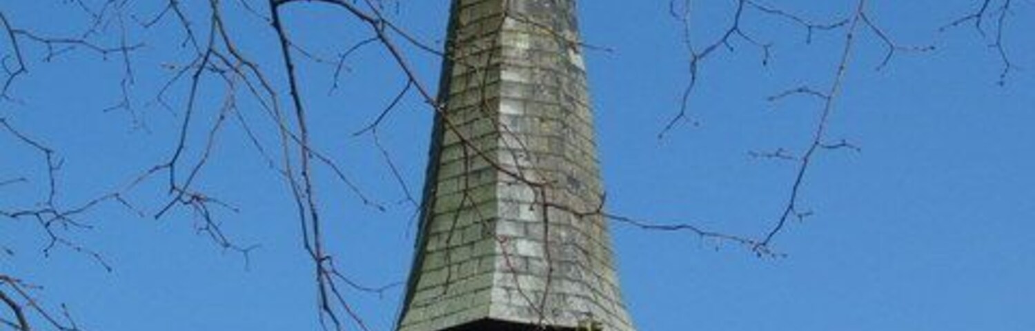 Um alto campanário de igreja com telhado pontiagudo e uma cruz no topo.