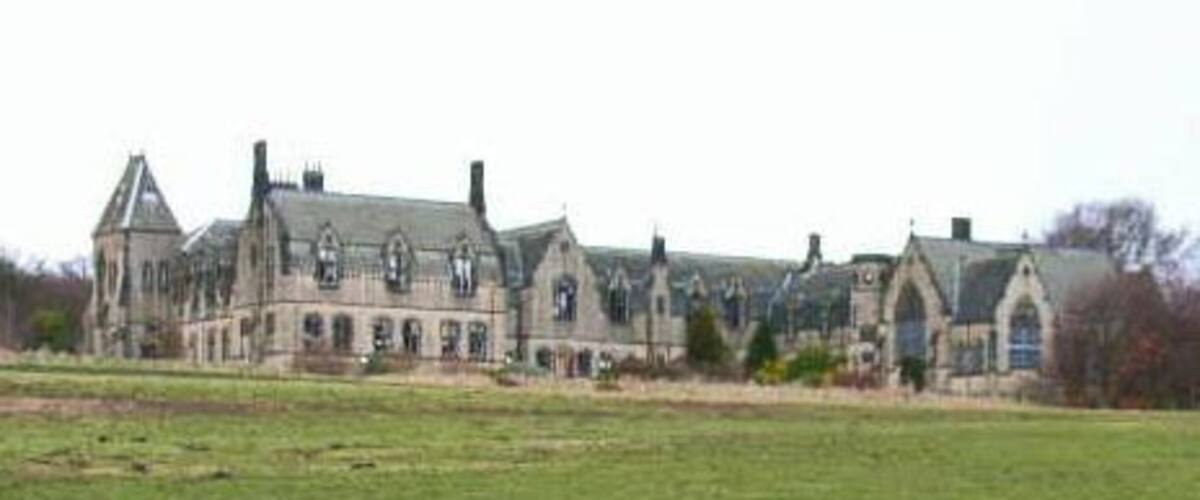 A large, historic building with multiple chimneys and a large lawn in front.