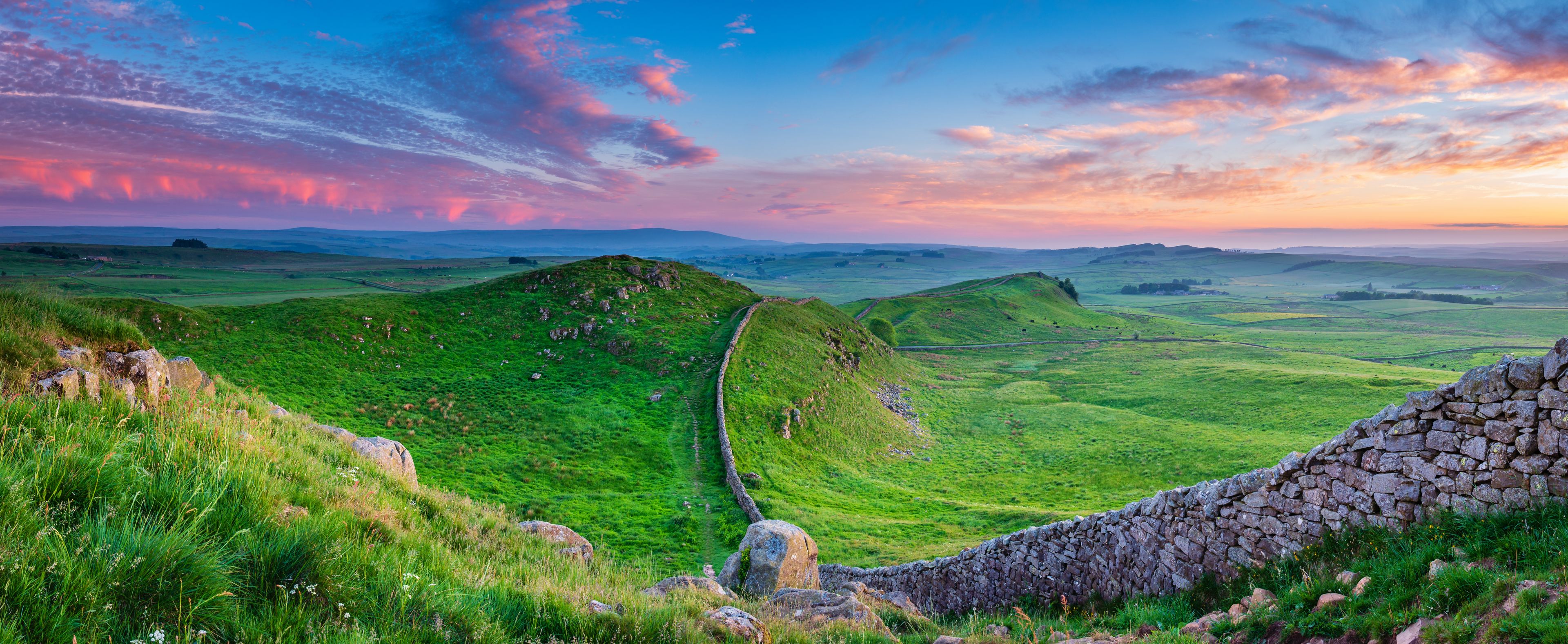 A stone wall, green hills, and a winding path.