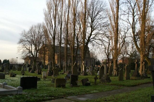 A cemetery with numerous tombstones and bare trees.