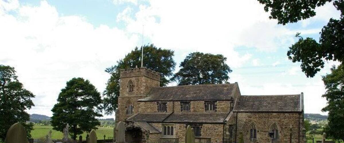 A church with a tower and stone walls, surrounded by a cemetery with headstones.
