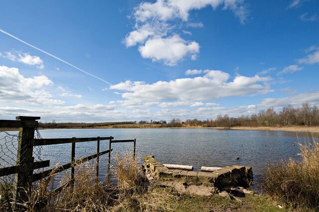 A calm lake with a wooden fence and a stone structure in the foreground.