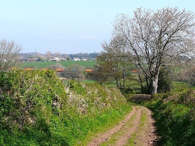 Public footpath to Carleton Mill View across the valley of the River Petteril, with a goods train on the West Coast Main Line. Carleton is in the distance.