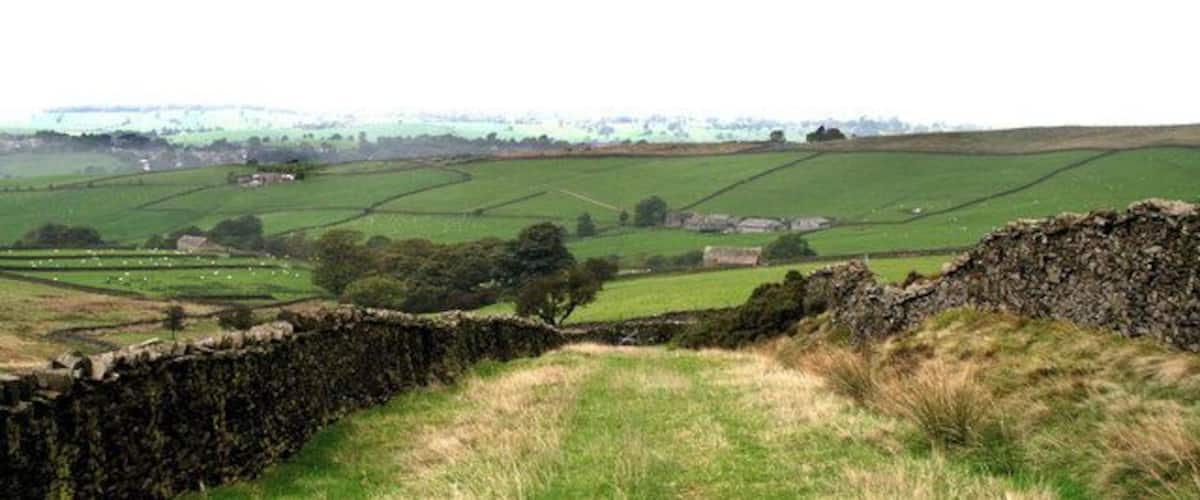 A stone wall, green fields, and distant buildings in a rural landscape.