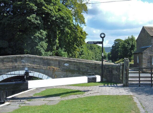 A stone bridge with a white arch, a signpost with directions, and a house in the background.