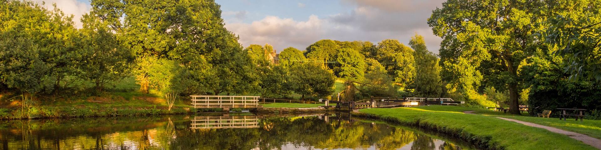 A calm river reflecting trees and a bridge.