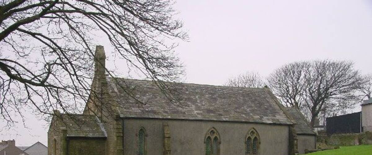 A church with a steep roof and arched windows on a grassy hill.