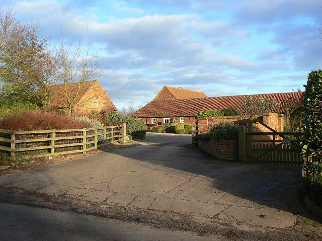 A rural road leading to a farm with stone walls and a red-roofed barn.