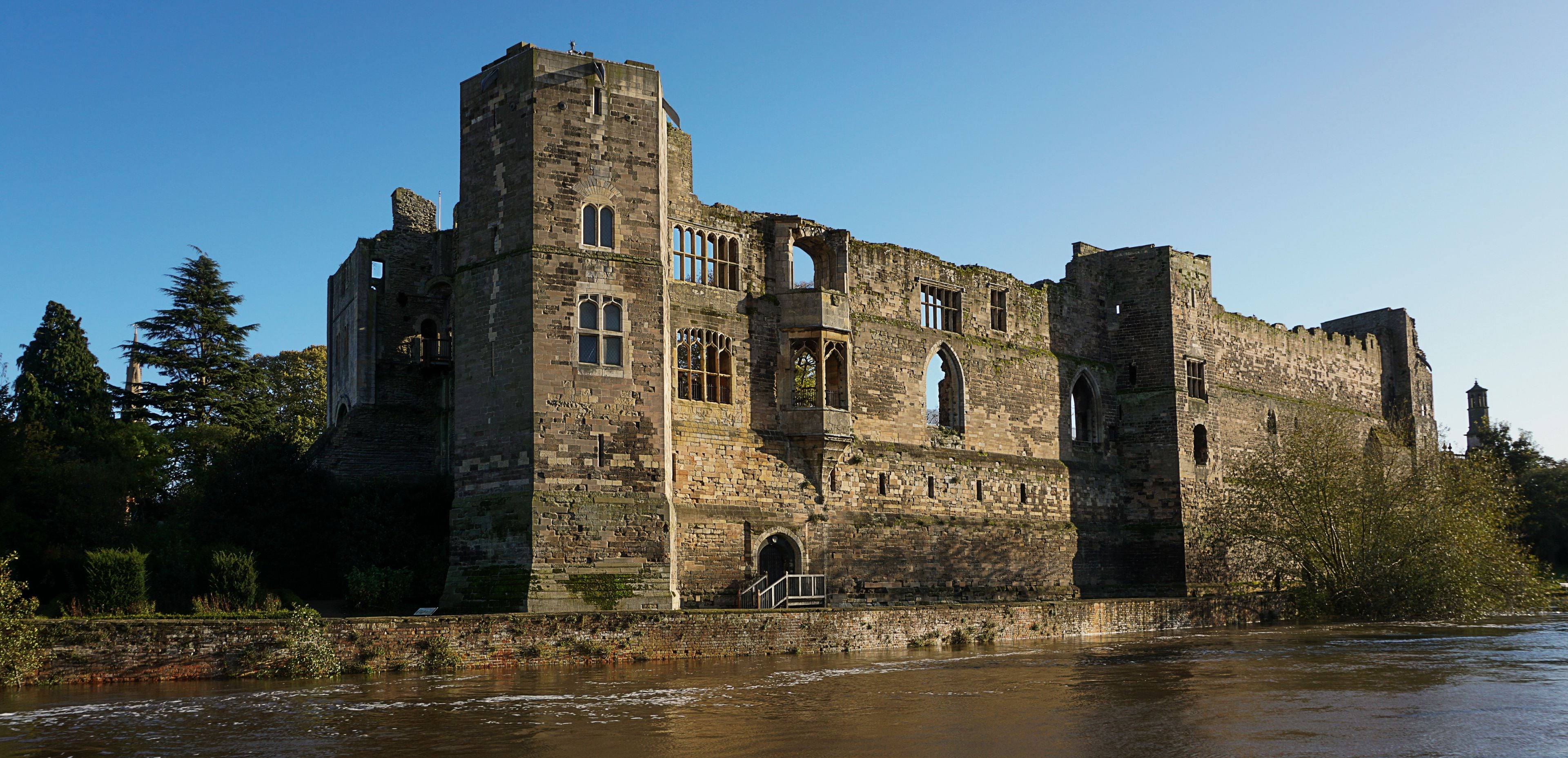 A historic castle with multiple towers and arched windows, situated by a river.