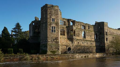 A historic castle with multiple towers and arched windows, situated by a river.