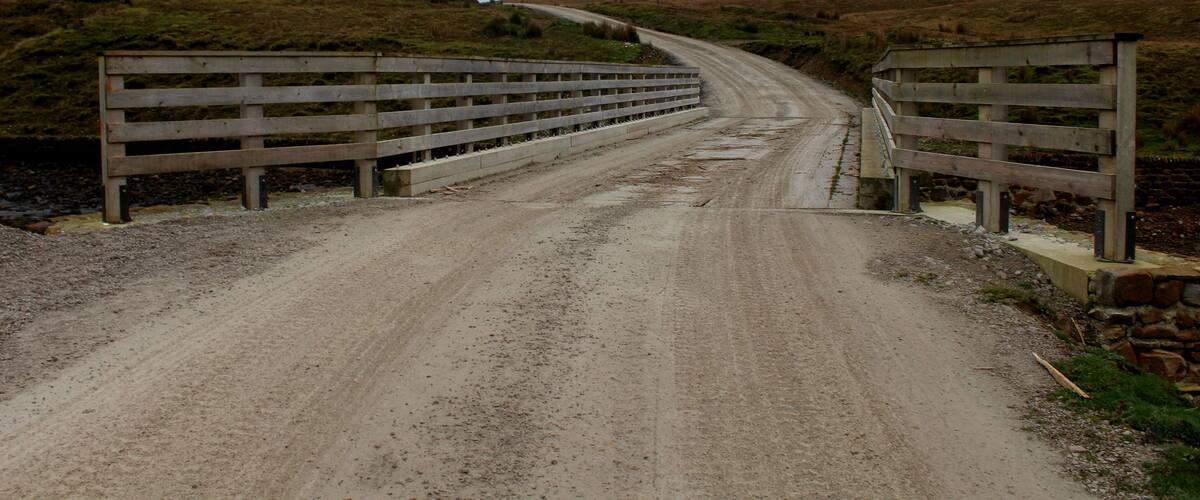 A gravel road leading to a wooden bridge over a body of water.