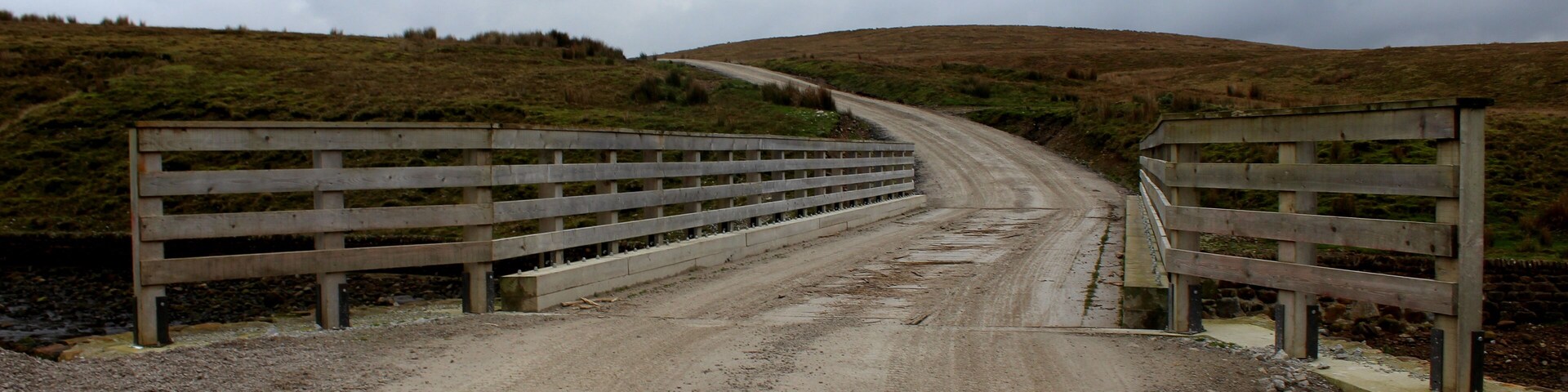 A gravel road leading to a wooden bridge over a body of water.