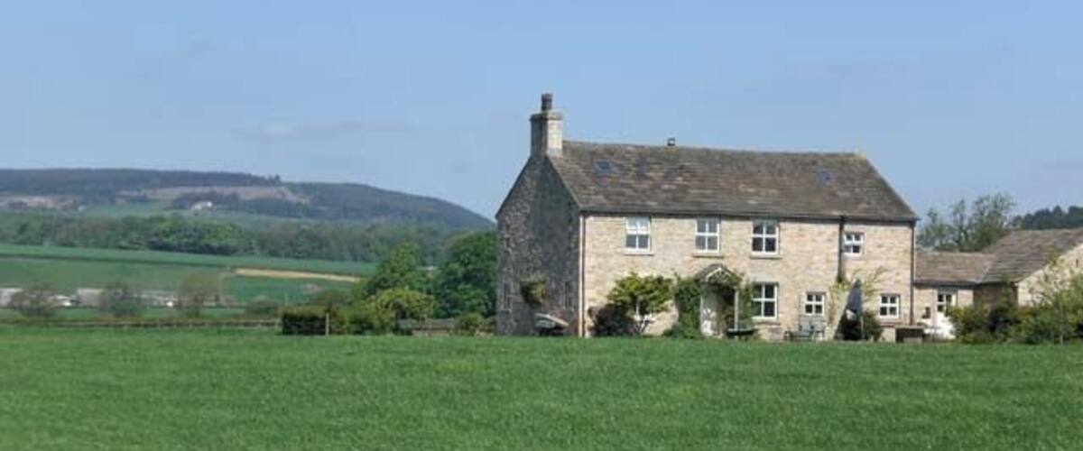 A stone house with a sloped roof in a green field.