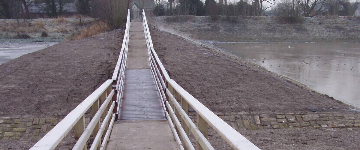 A concrete bridge with white railings leading to a body of water.