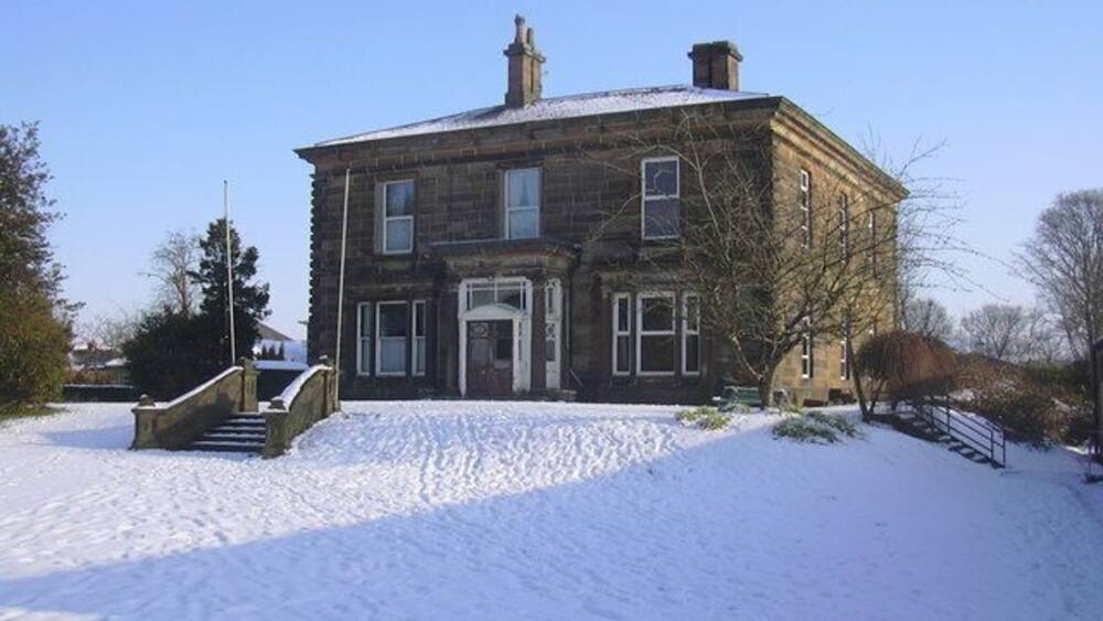 A large stone building with a snow-covered lawn and a small bridge leading to the entrance.