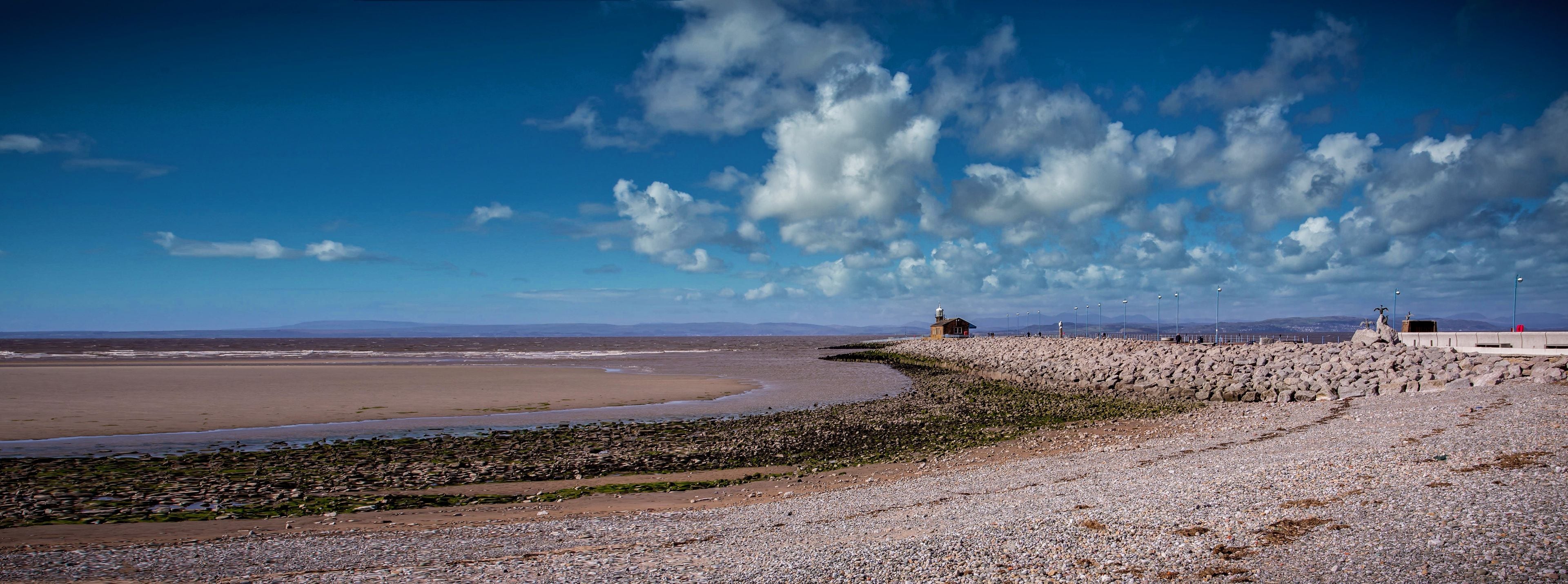 A rocky beach with a lighthouse and distant mountains under a partly cloudy sky.