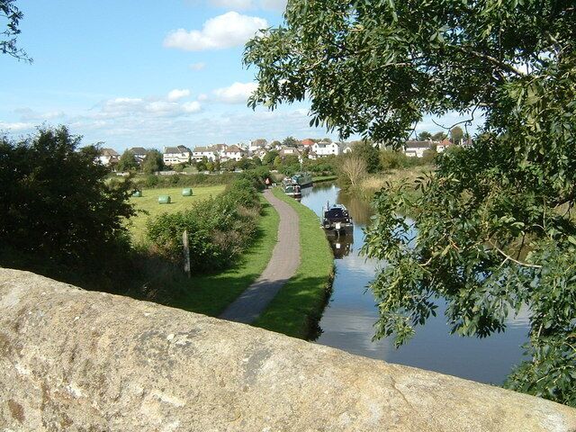 A canal with a narrow path alongside, a boat, and houses in the background.