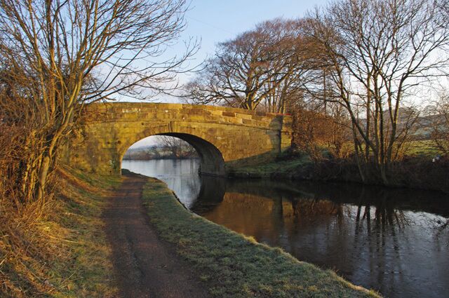 A stone bridge over a calm river, surrounded by bare trees and a grassy path.