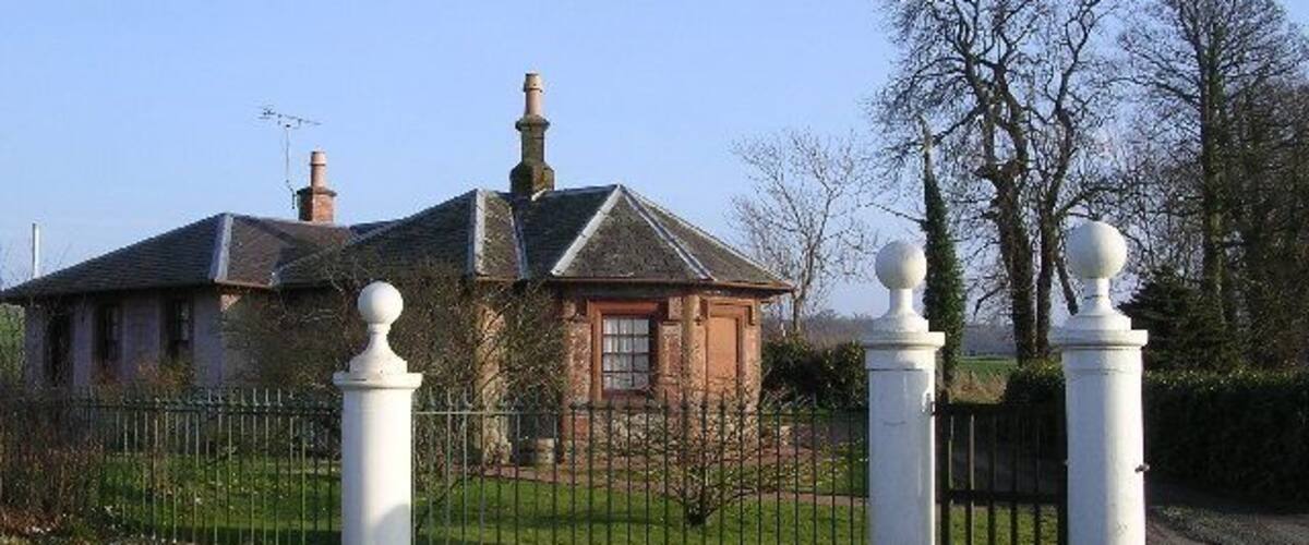 A house with a brick facade, a metal fence, and a white gate with spherical finials.