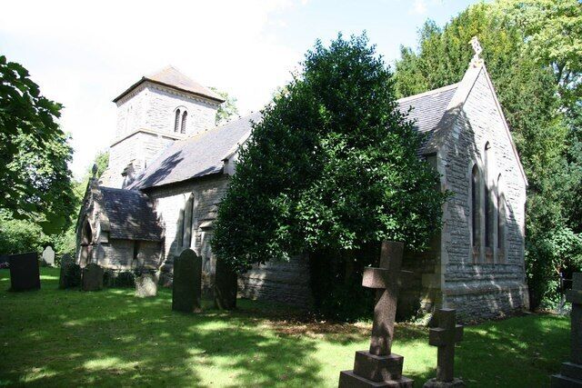 A church with a stone facade, surrounded by trees and a grassy area.