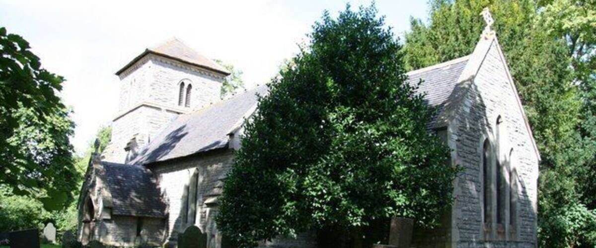 A church with a stone facade, surrounded by trees and a grassy area.