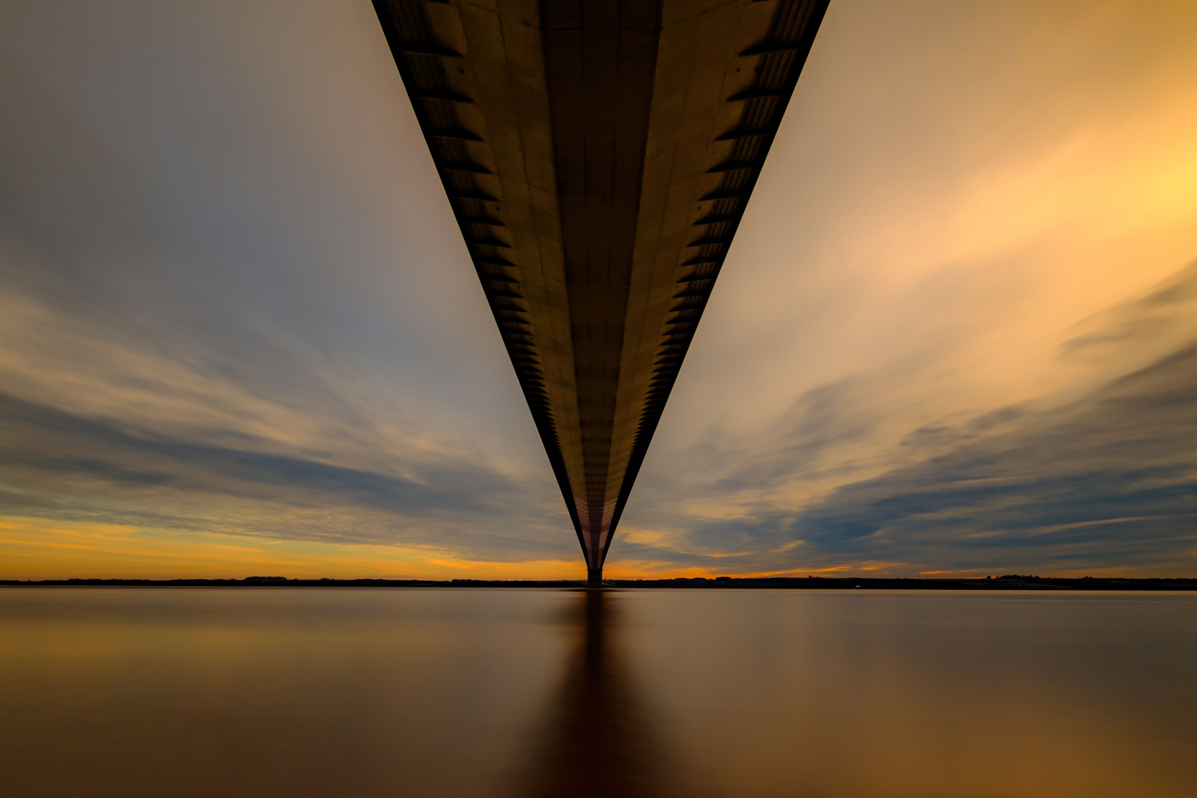 Un puente con un diseño de arco simétrico sobre un cuerpo de agua tranquilo al atardecer.