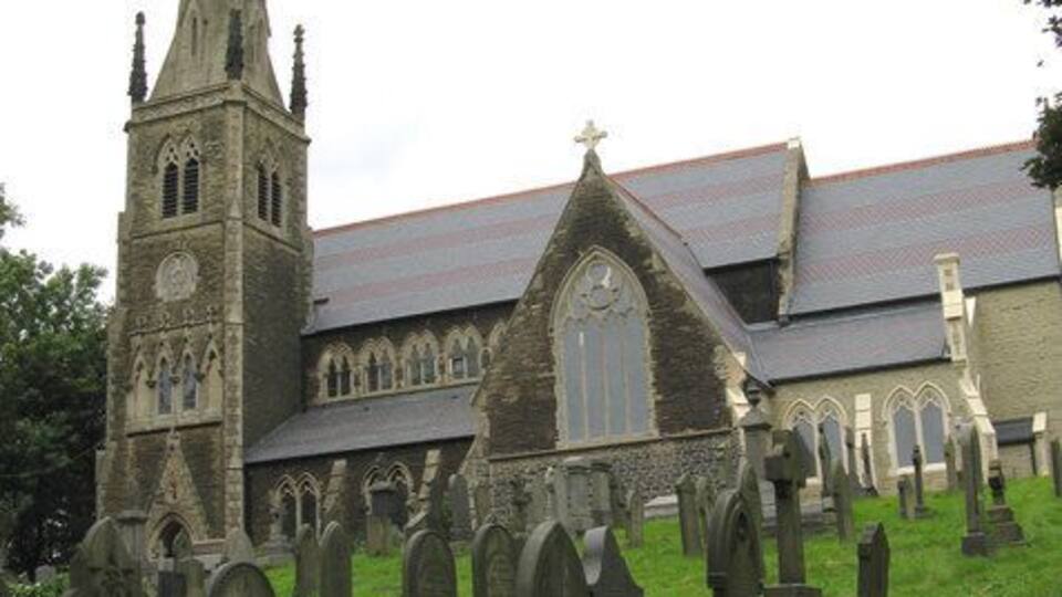 A church with a tall spire and a graveyard with numerous headstones.